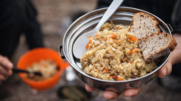 Hiker holding a metal bowl of quinoa and beans with bread during a backcountry meal stop.