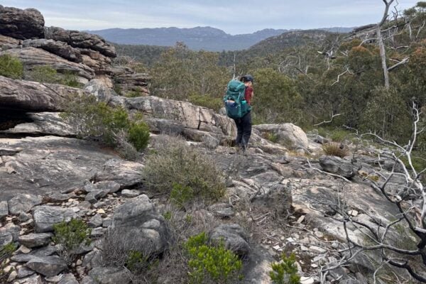Female hiker with a large backpack navigating rocky terrain in the grampians, lagging behind the group. Depicts a minor ankle roll and reduced pace affecting group movement.